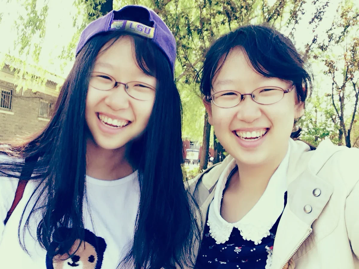 The same selfie after a face swap: the woman in the purple cap now has the face of the woman in glasses, including her glasses and wide smile, so the same face appears twice.