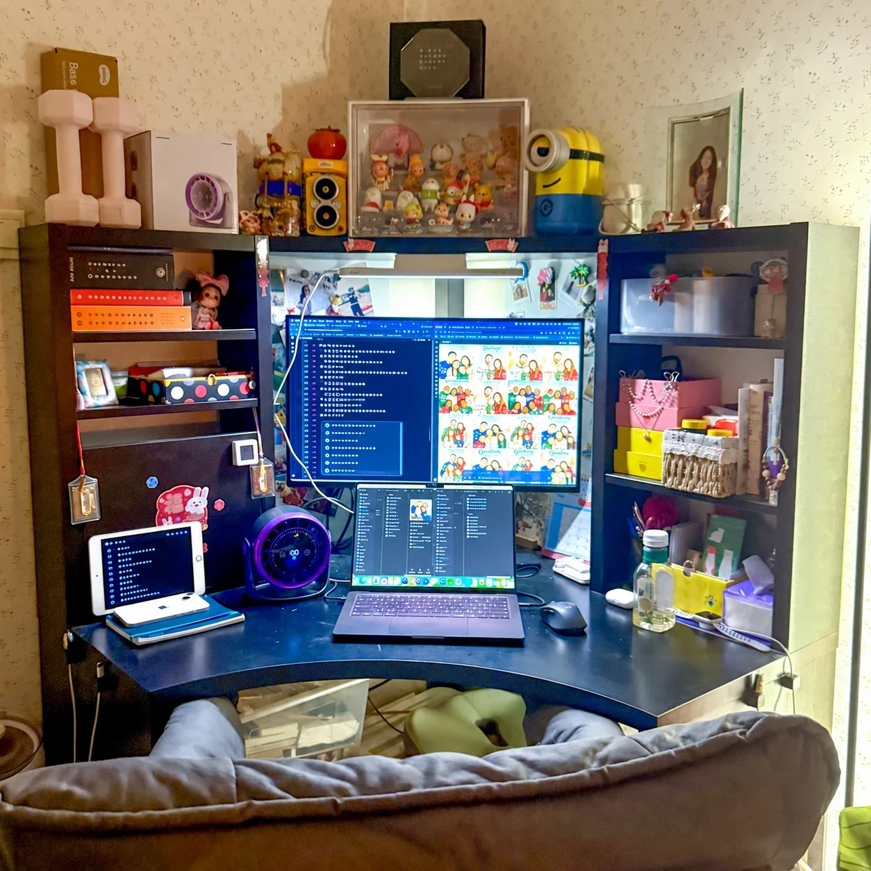 My home workspace, with a large monitor showing card illustrations, a laptop, and shelves of books and keepsakes.